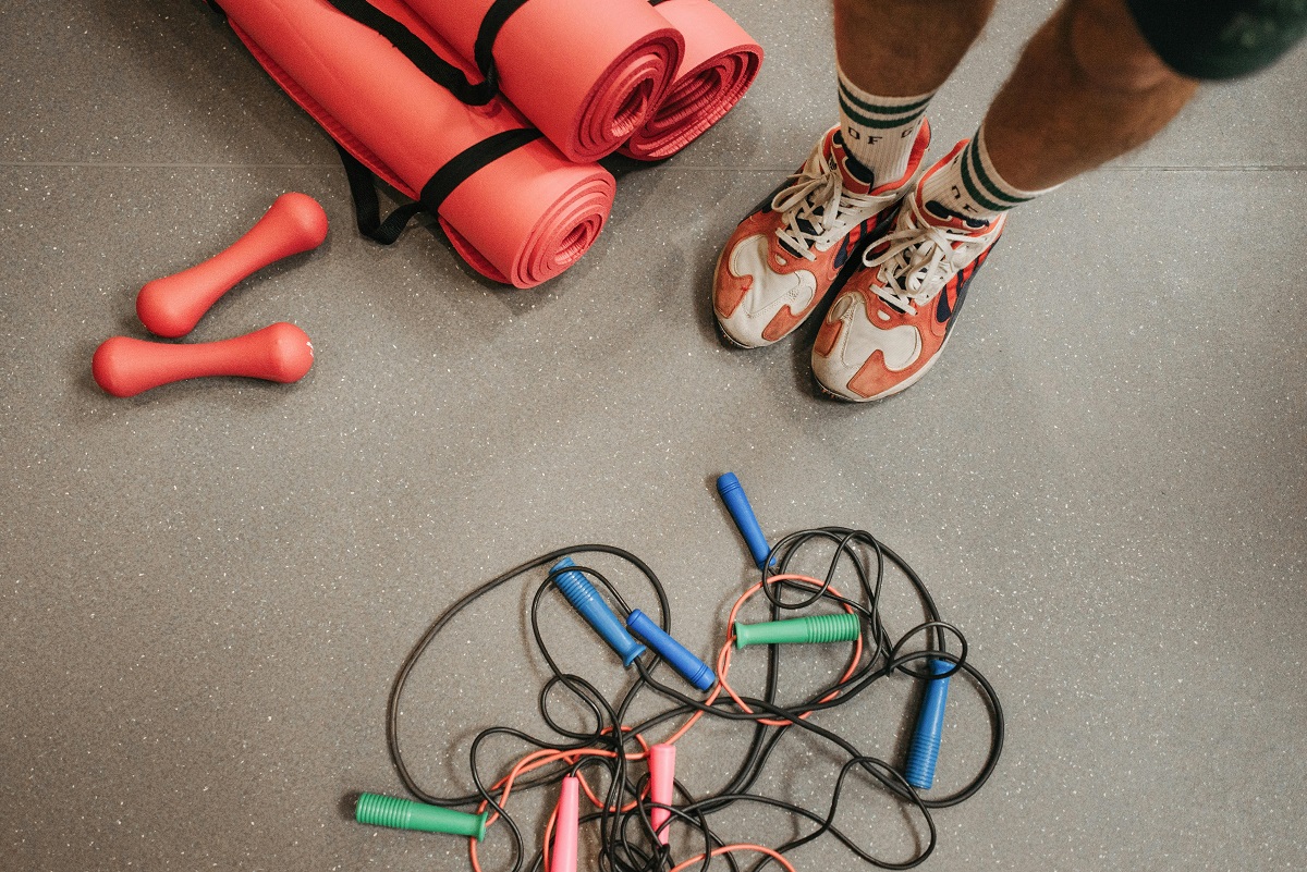 man's feet in sneakers surrounded by jump ropes, yoga mats, and weights