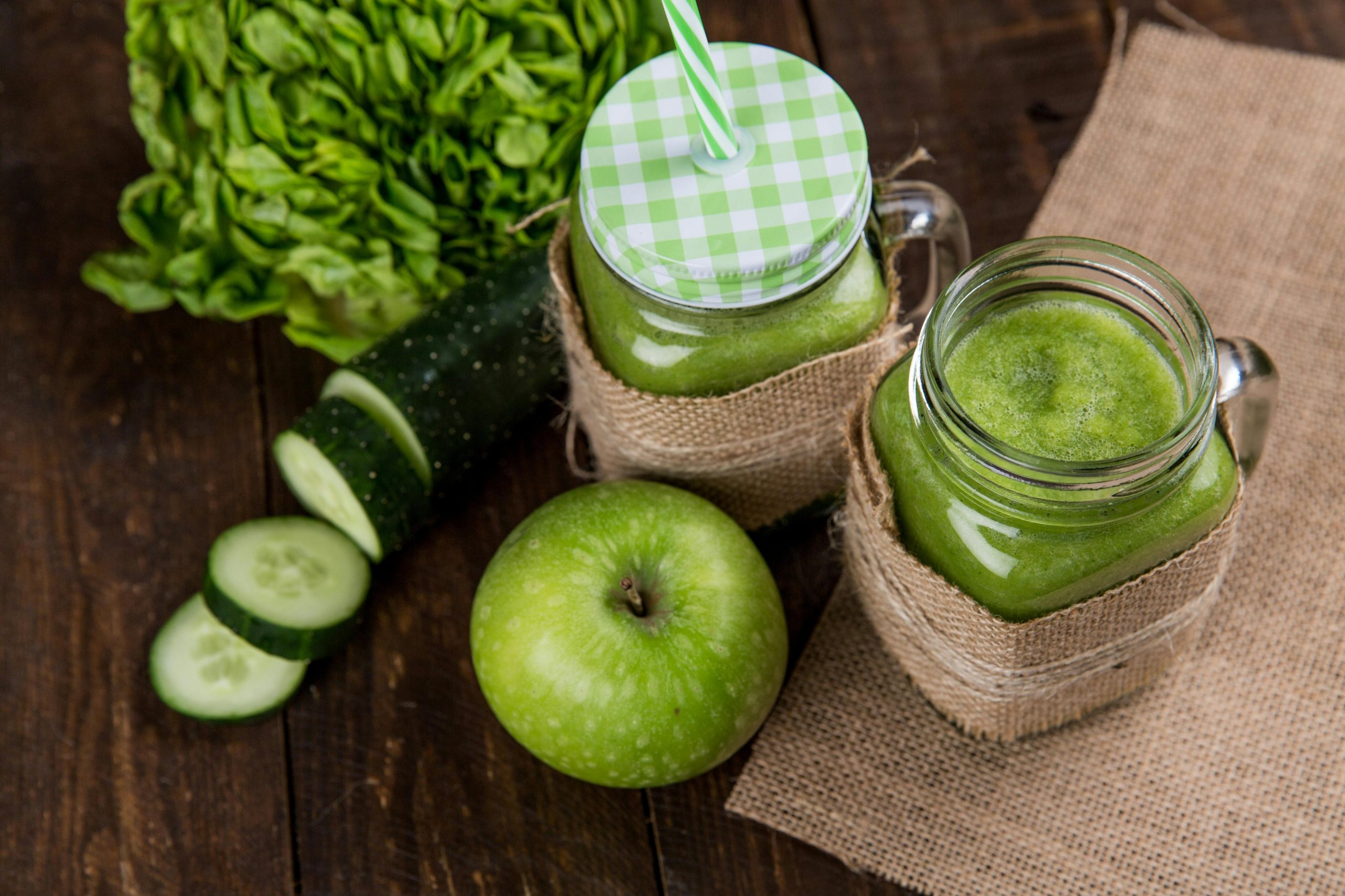 green smoothies in mason jars next to a green apple and cucumber